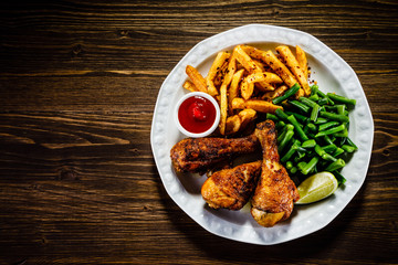 Grilled chicken drumsticks with vegetables on wooden background