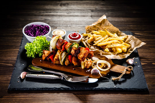 Kebabs - grilled meat with french fries and vegetables on wooden background 