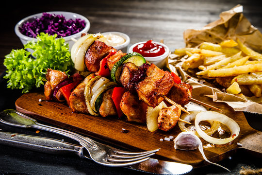 Kebabs - grilled meat with french fries and vegetables on wooden background 