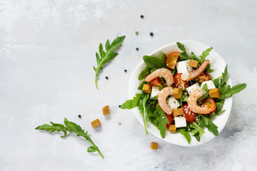 Festive appetizer. Salad with shrimps, feta cheese, arugula, cherry tomato and sesame on a stone or slate background. Top view.