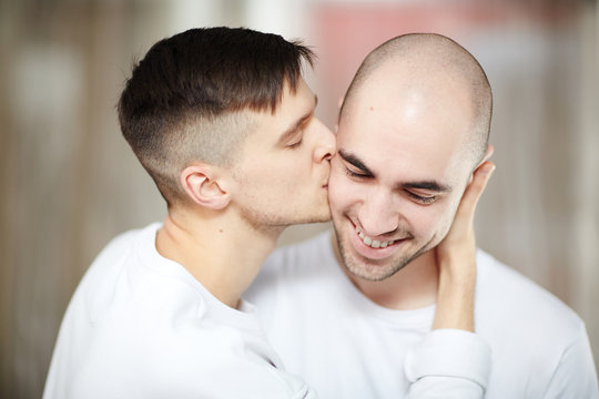 One of amorous guys kissing his partner on cheek and embracing him
