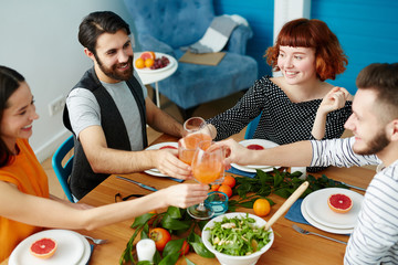 Two happy couples toasting with glasses of juice over served table with healthy food