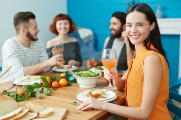 Pretty young housewife with wineglass of juice sitting by served table with her guests