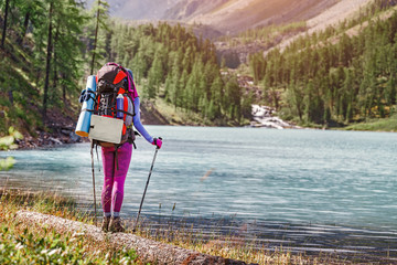 girl hiker standing on a rock and looking at the lake in Altai mountains