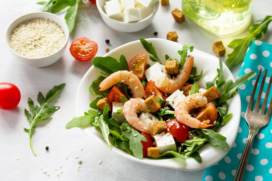 Festive appetizer. Salad with shrimps, feta cheese, arugula, cherry tomato and sesame on a stone or slate background.