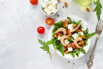 Festive appetizer. Salad with shrimps, feta cheese, arugula, cherry tomato and sesame on a stone or slate background. Top view.