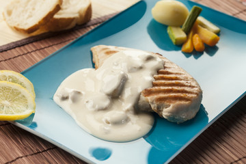 grilled chicken breast with mushroom sauce on blue plate , modern presentation with vegetables