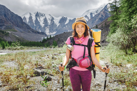 Young happy woman with backpack walking along the footpath trail alone in the mountains, the concept of outdoor activities and adventures in nature