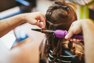 Close-up of a male hairdresser making curls at long brown hair with curling irons.