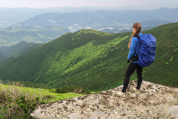 Woman with backpack standing on the edge of the stone looks into the distance
