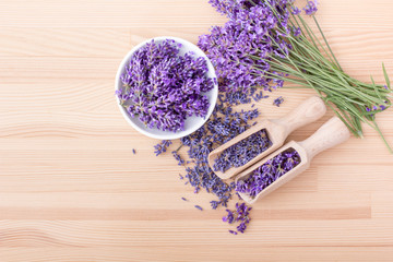 Fototapeta premium Top view of a bowl and wooden spoons with dried and fresh lavender flowers and a bouquet of lavender on a wooden background 