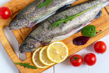 Fresh raw trout fish and food ingredients on wooden board.