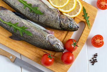 Fresh raw trout fish and food ingredients on wooden board.