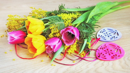 Tulips, mimosa and Easter decorations on wooden background.