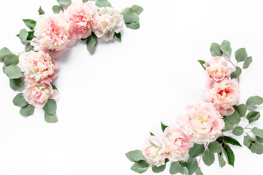 Floral frame wreath made of pink and beige peonies flower buds, eucalyptus branches and leaves isolated on white wooden background. Flat lay, top view. Frame of flowers. 