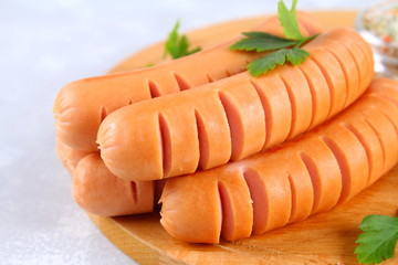 Fried chopped sausages on a wooden board on a gray concrete table.
