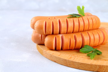 Fried chopped sausages on a wooden board on a gray concrete table.