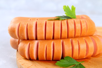 Fried chopped sausages on a wooden board on a gray concrete table.