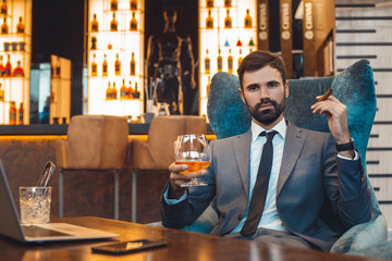 Businessman sitting in a business center bar smoking cigar and drinking whiskey