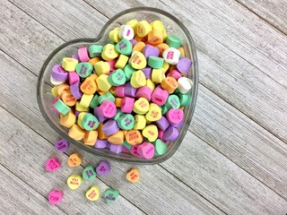 Valentine's Day candy hearts in a heart shaped glass dish on a distressed wood surface