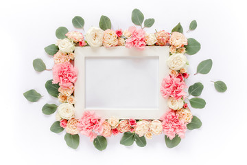 White frame decorated with pink roses flowers and leaves of eucalyptus. Flat lay, top view. Floral...