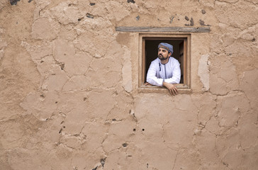 arab man in traditional omani outfit in an old castle, looking out of a window