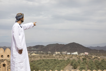arab man in traditional omani outfit in an old castle pointing to the distance