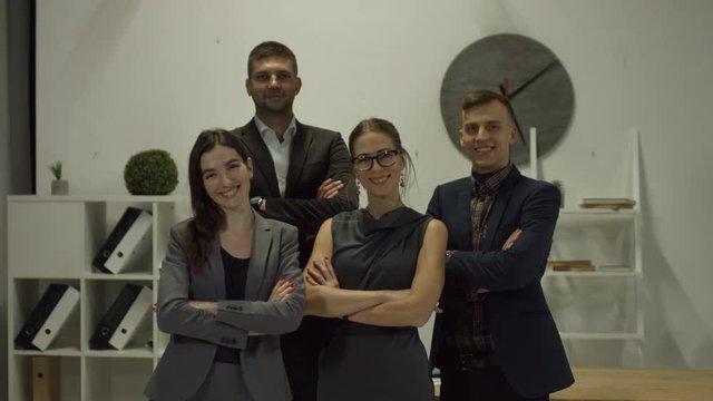 Portrait of smiling confident business team standing with arms crossed in modern office. Successful happy business people with folded hands posing in office and looking at camera with toothy smiles.