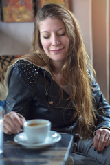 Cheerful young casual lady drinking her coffee in a coffee shop, enjoying some free time for herself