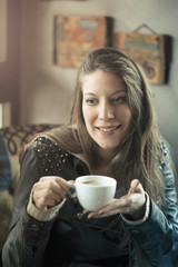 Cheerful young casual lady drinking her coffee in a coffee shop, enjoying some free time for herself