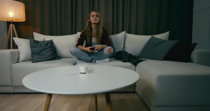 Young adult Caucasian female sits on couch, turning on TV screen. 4K UHD