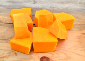 A group of cut and slice butternut squash chunks on a wooden board