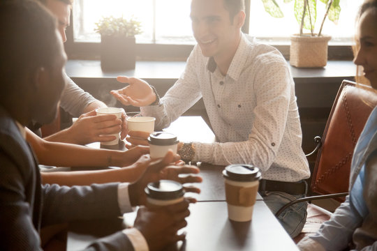 Multi Ethnic Group Of Happy Friends Drinking Coffee In Paper Cups Together In Cozy Cafe, Diverse Multiracial African And Caucasian Young People Talking Sharing Table Having Fun At Coffeehouse Meeting