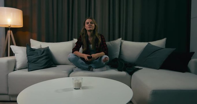 Young adult Caucasian female sits on couch, turning on TV screen. 4K UHD