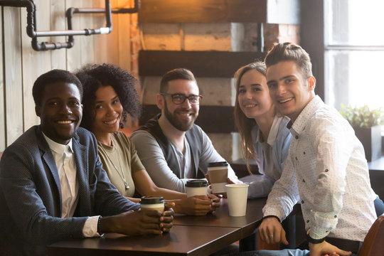 Happy multiracial friends group looking at camera having fun in cafe together, young african and caucasian people bonding sitting at coffeehouse table, smiling diverse millennial students portrait