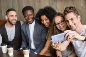 Young caucasian man making selfie on smartphone at meeting with multiracial millennial friends,...