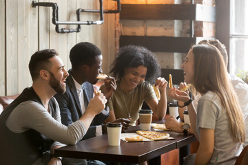 Multiraciale gelukkige jonge mensen die pizza eten in pizzeria, zwart-witte vrolijke vrienden lachen genietend van een maaltijd die plezier heeft om samen aan de tafel van het restaurant te zitten, diverse vrienden delen de lunch tijdens de vergadering