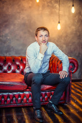 Obraz premium Stylish man in white shirt , sitting in leather red sofa