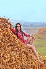 A model in a bright red dress sits on a hay