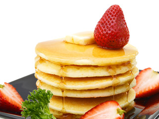 Plate of pancakes with maple syrup topped with strawberry