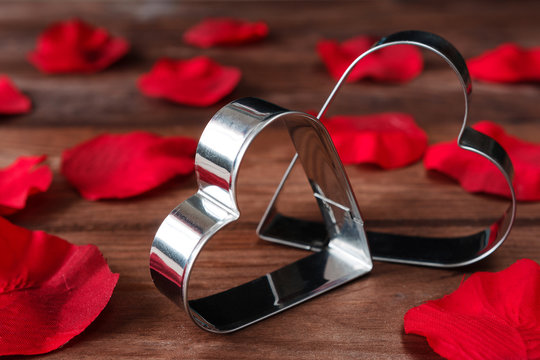 Two metal shiny hearts on a wooden background with red flower petals in vintage style with copy space