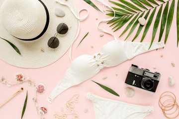 Obraz na płótnie Canvas Feminine white swimsuit beach accessories, tropical palm leaf branches on pink background. Travel vacation concept. Summer background. Road frame set. Traveler accessories. Flat lay, top view. 