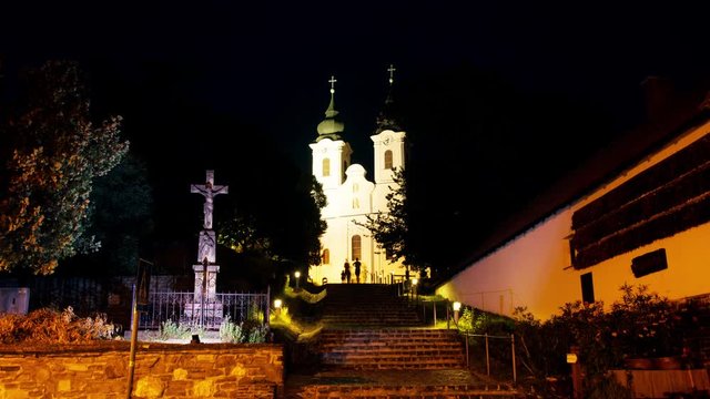 Tihany, Hungary. Tihany Abbey is a Benedictine monastery in Hungary at night with illuminated steps and cross. Dark black sky, popular landmark. Time-lapse with silhouettes