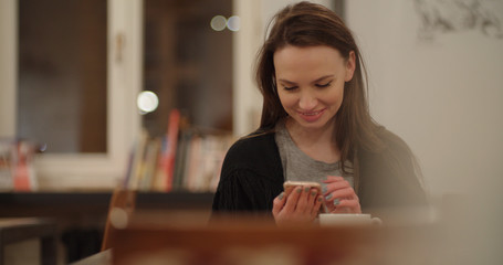 Young cheerful woman using cell phone in restaurant.