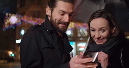 Young happy couple using smartphone at night. Young beautiful couple share memories and pictures on social media with online mobile app.
