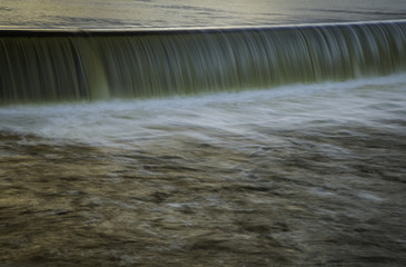 A river flowing through the weir in the early evening light