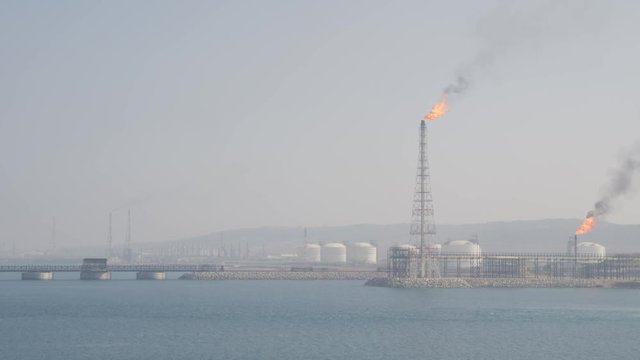 Flare stack of petrochemical refinery on sea shore in haze