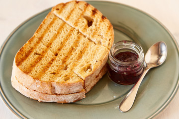 Toast with cherry jam on a white wooden table. Fried bread on a gray shiny plate.