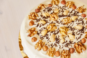 A large delicious pie with walnuts. Homemade pie with white topping and chocolate chips on a white wooden table.
