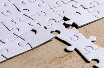 the unexpected solution, white jigsaw/puzzle with a row in wrong position, over  wooden table...